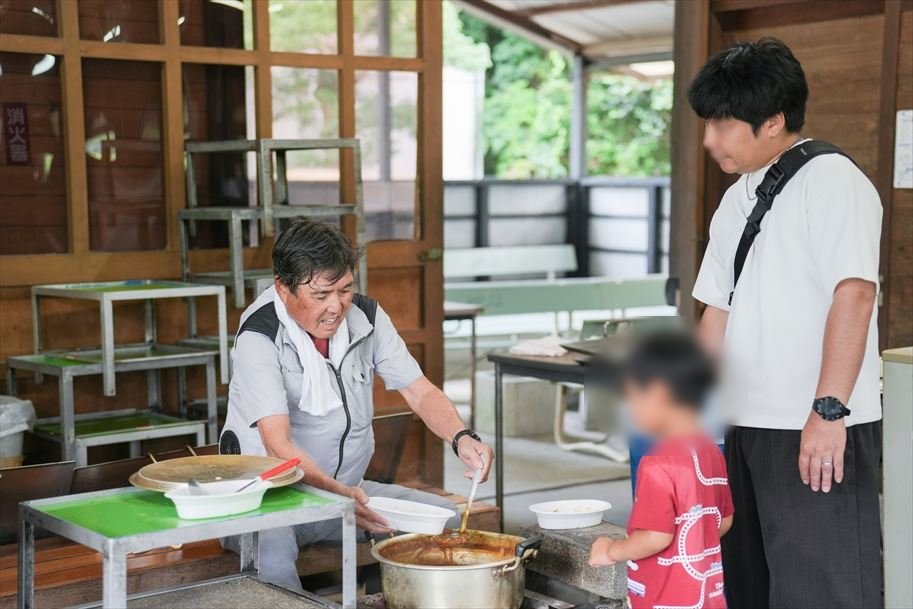 スタッフが大鍋からカレーをよそって手渡す