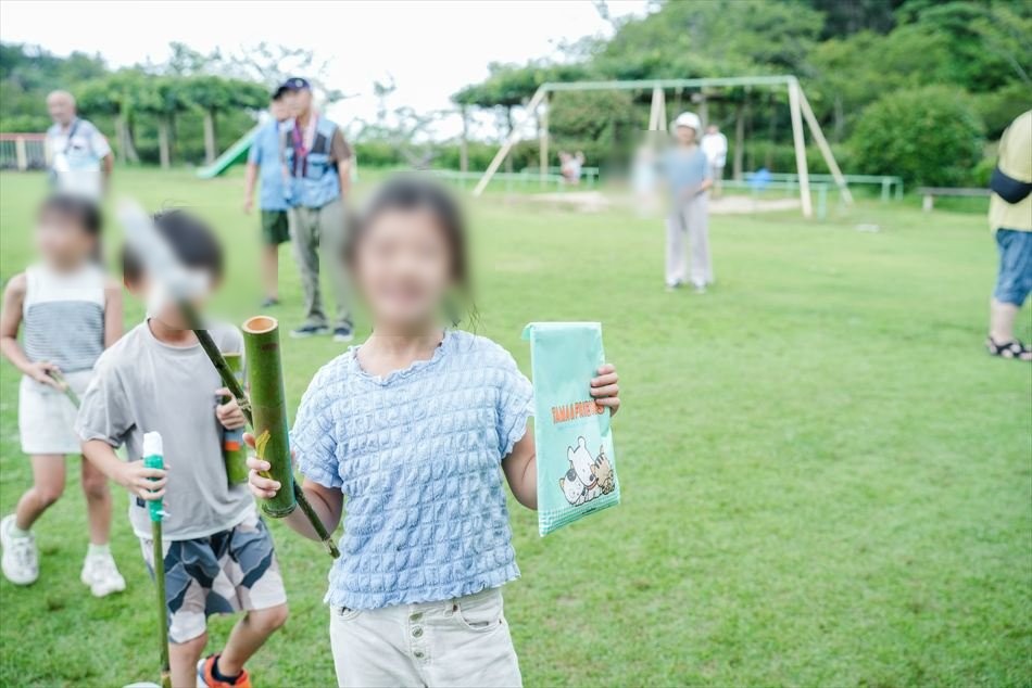 できあがった竹の水鉄砲を持って芝生広場に立つ子ども