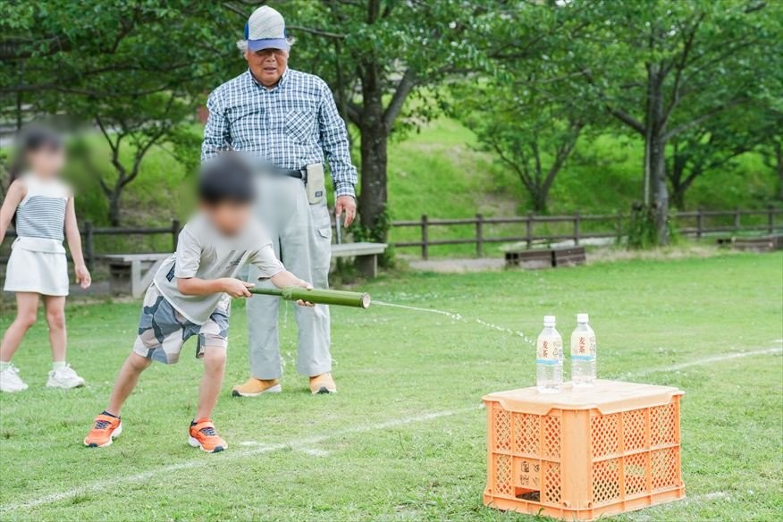 芝生広場でペットボトルの的をねらう子どもと見守るスタッフ