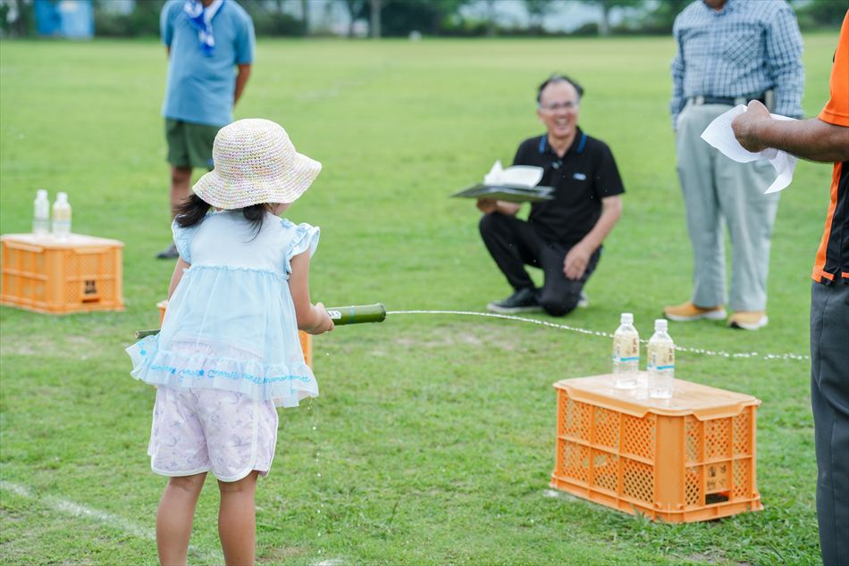 麦わら帽子の女の子が竹の水鉄砲で的あてに挑戦