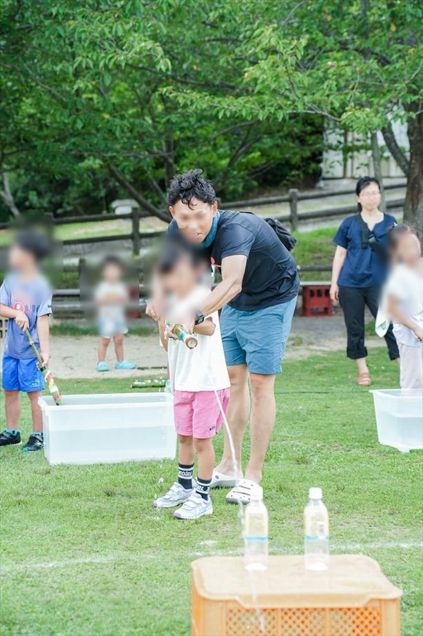 水をくみながら、大人が子どもの手を支えて水鉄砲を構える