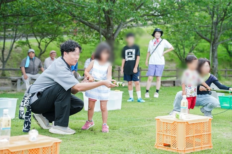 芝生広場でスタッフが子どもの手を支えて水鉄砲の向きを教える